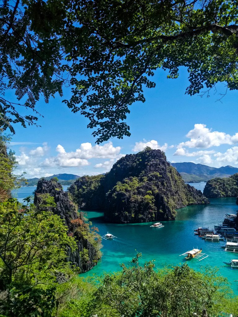 A striking, vertical photograph used as an Instagram Reel cover, capturing a person in a traditional outrigger boat (bangka) on the clear, turquoise water of Kayangan Lake in Coron, Palawan, Philippines